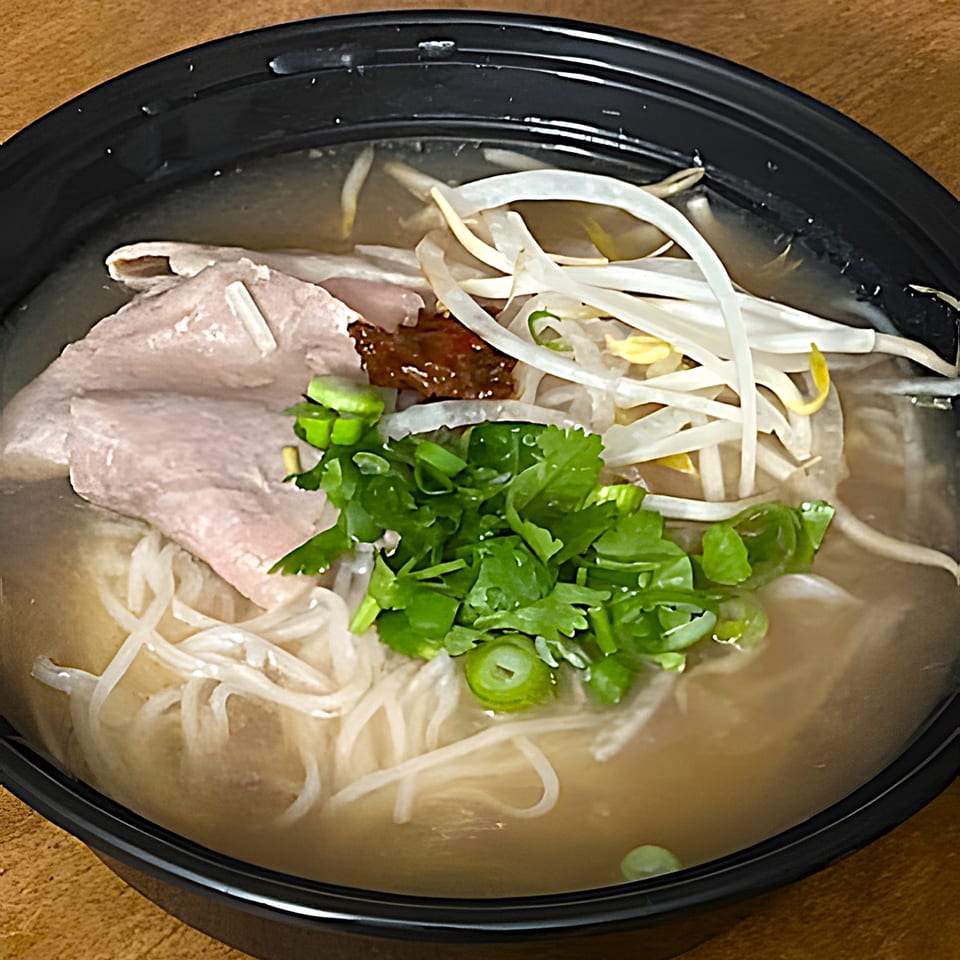 Close-up of I Love Pho's pho with beef, noodles, bean sprouts, and fresh herbs in a black bowl.