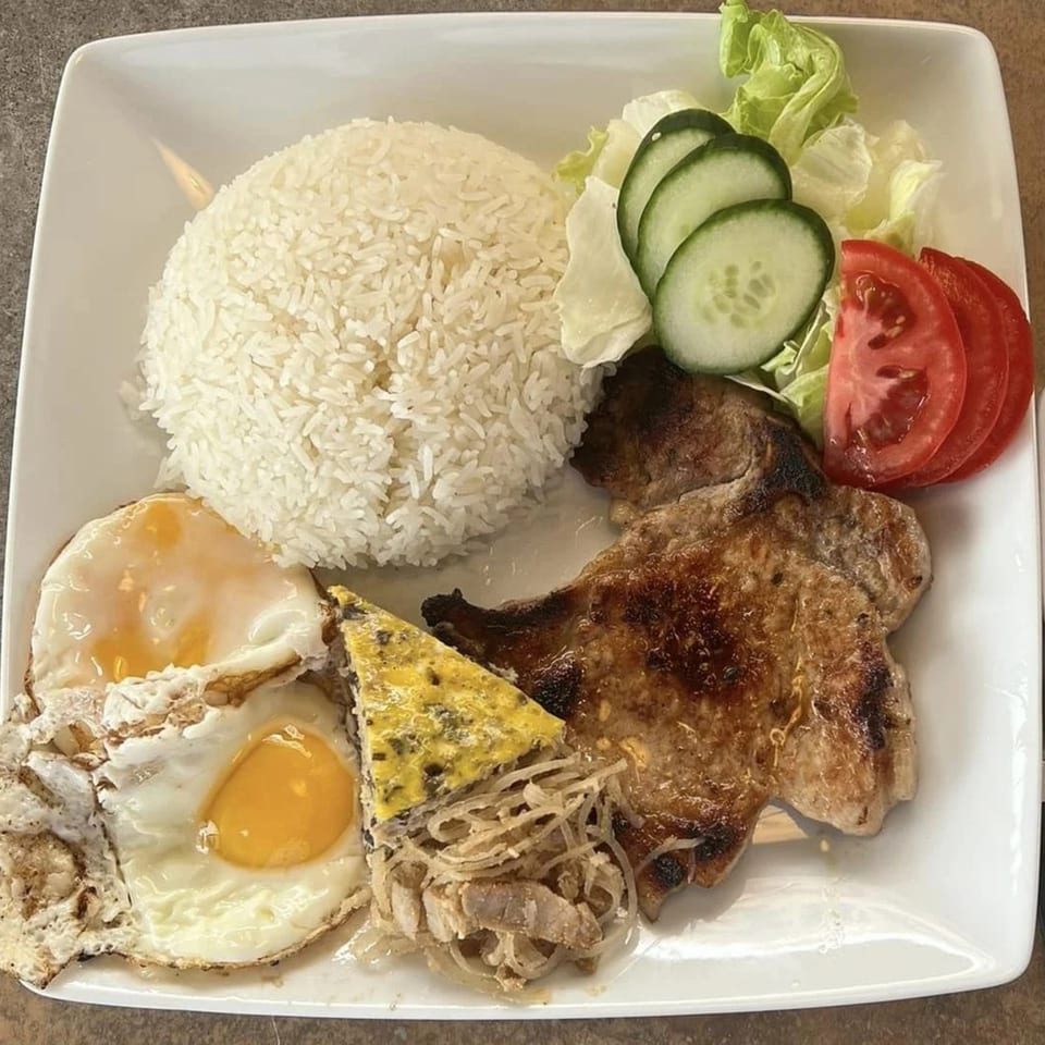 Vietnamese grilled pork chop with fried eggs, rice, and a side salad on a white plate.