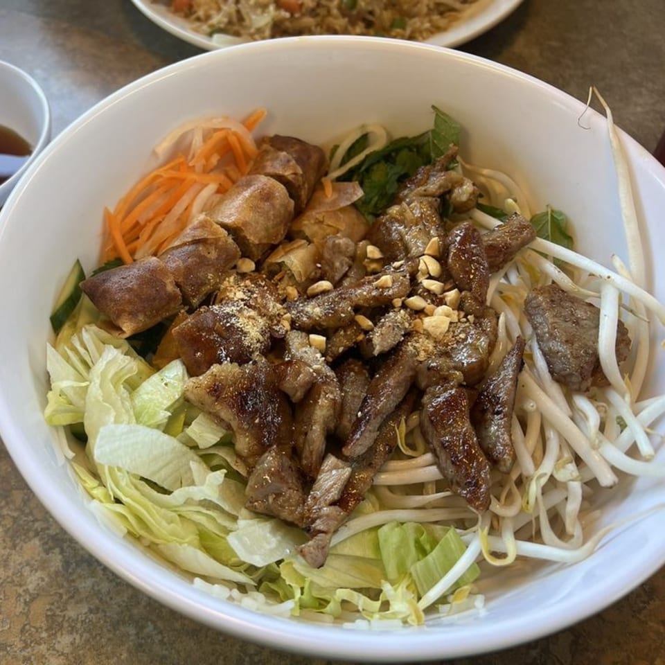 A Vietnamese vermicelli bowl with grilled beef, crispy spring rolls, fresh vegetables, and peanuts.