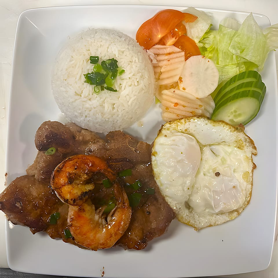 Vietnamese grilled pork and shrimp with rice, fried egg, and a side salad on a white plate.